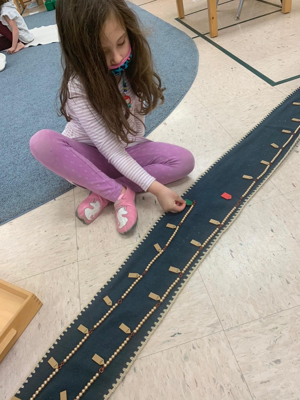 Royersford Campus: A child is busy working with one of our iconic materials - The Bead Chains. She is learning to count 1 to 1000 using the long bead chain.