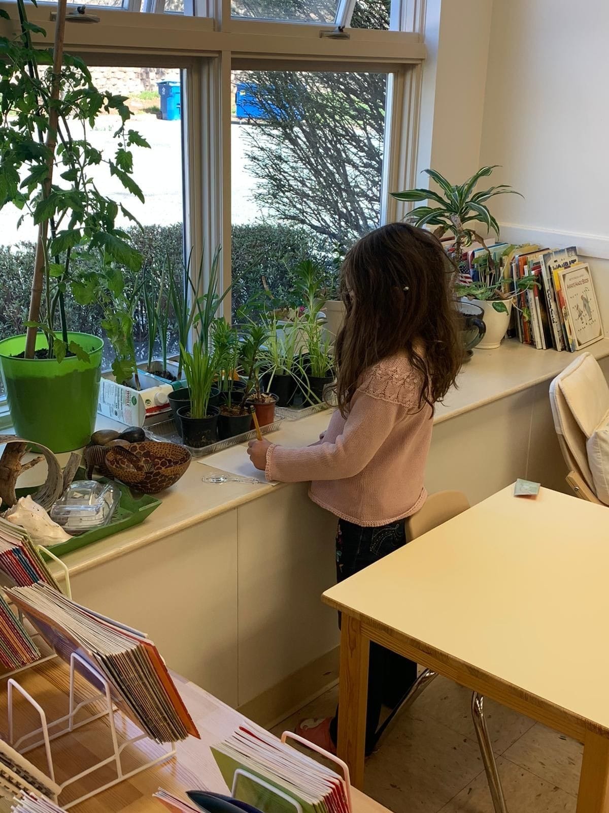 A child examining the indoor plants using a magnifying glass and writing a journal about it.
